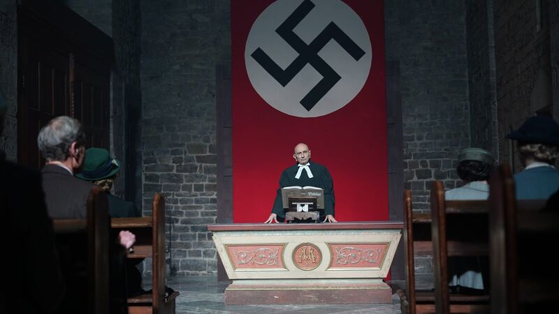 Bonhoeffer film still: a pastor preaches beneath a swastika banner